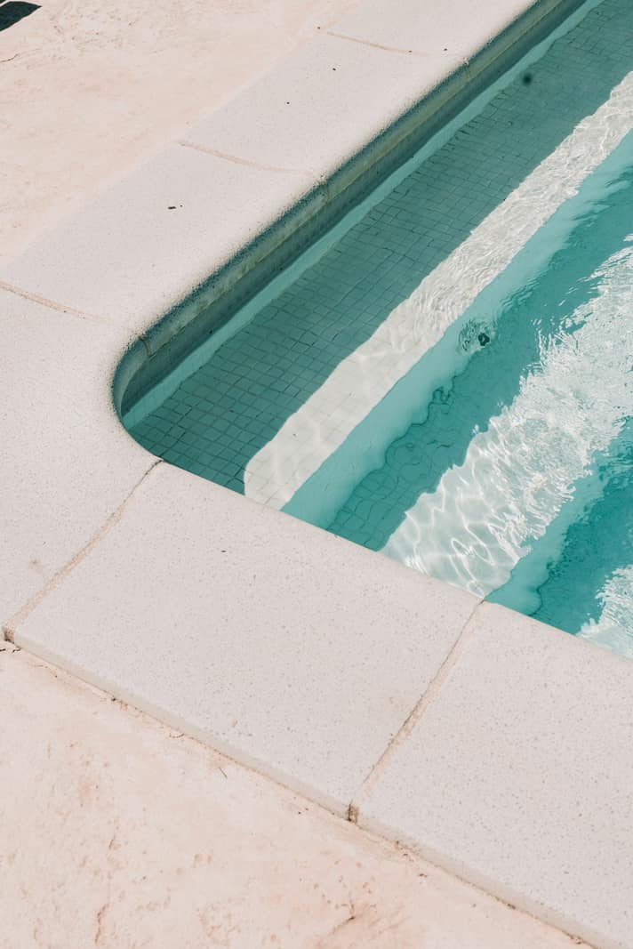 Entry steps and bench of a pool finished in pale plaster, with clear blue water